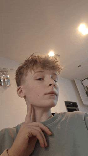 a young man in a blue shirt has his finger on his chin