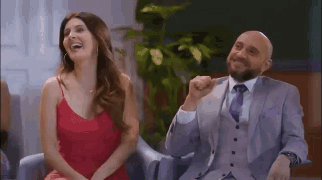 a man in a suit and tie is sitting next to a woman in a red dress who is laughing .