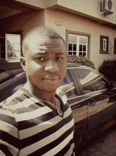 a man in a striped shirt stands in front of a black car