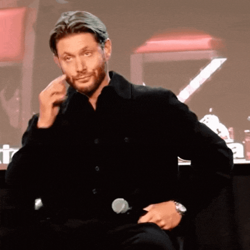 a man in a black shirt is sitting in front of a microphone and making a face