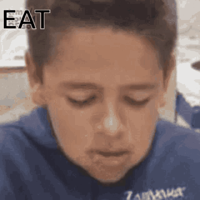 a boy in a blue shirt with the word eat written on his forehead