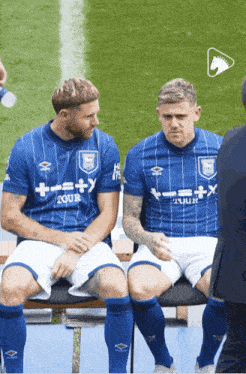 two soccer players are sitting on a bench and one has a shirt that says tour