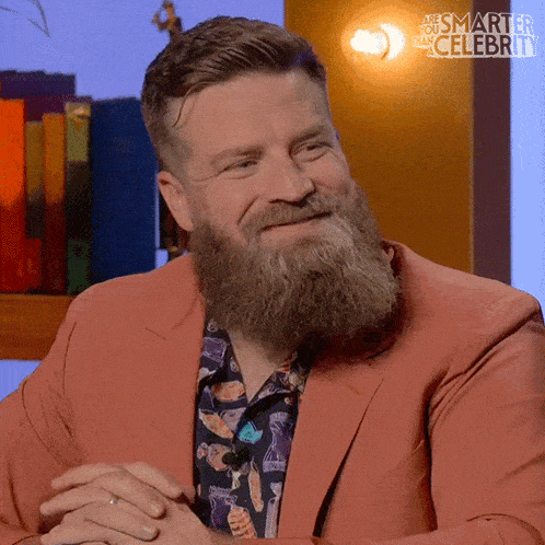 a man with a beard is wearing a pink suit and a shirt that says " smarter than celebrity "