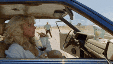 a woman is sitting in a car with a bag of prada on the dashboard