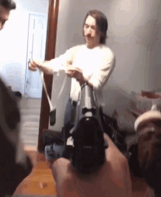 a man in a white shirt is pointing a gun at another man in a room