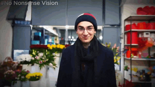 a man wearing glasses and a beanie stands in front of a shelf full of flowers with the words no nonsense vision visible
