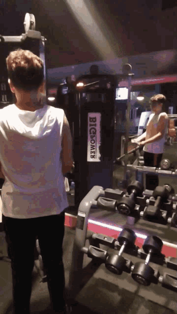 a man in a white tank top stands in front of a machine that says big boals
