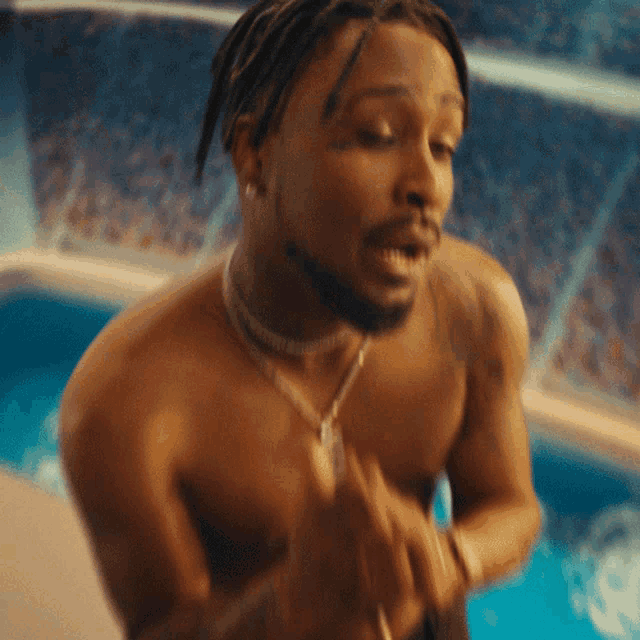 a shirtless man with dreadlocks is standing in front of a swimming pool