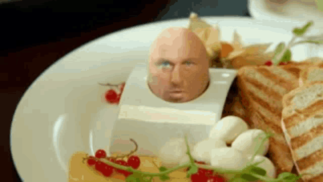 a plate of food with an egg with a man 's face sticking out of it .