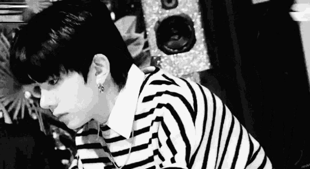 a black and white photo of a young man wearing a striped sweater and earrings .