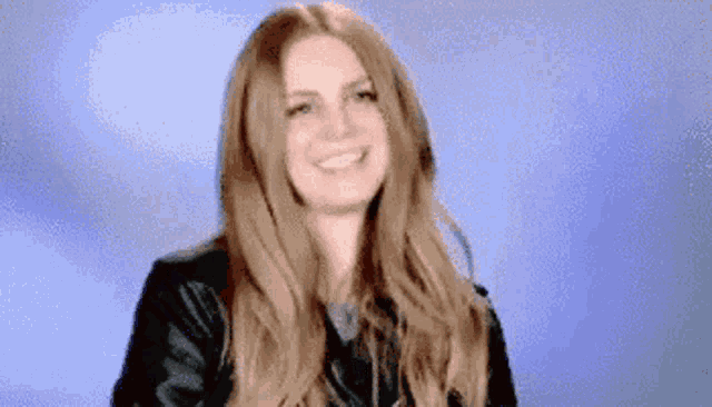 a woman with long hair is smiling and wearing a leather jacket .