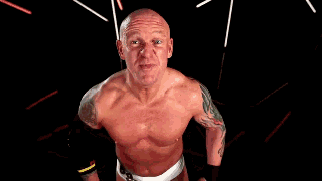 a shirtless wrestler with a tattoo on his arm is standing in front of a black background