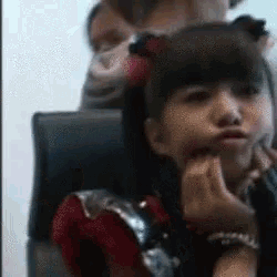 a little girl in a red and silver dress is sitting in a chair with her hands on her face .