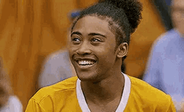 a young man in a yellow shirt is smiling in a basketball court .