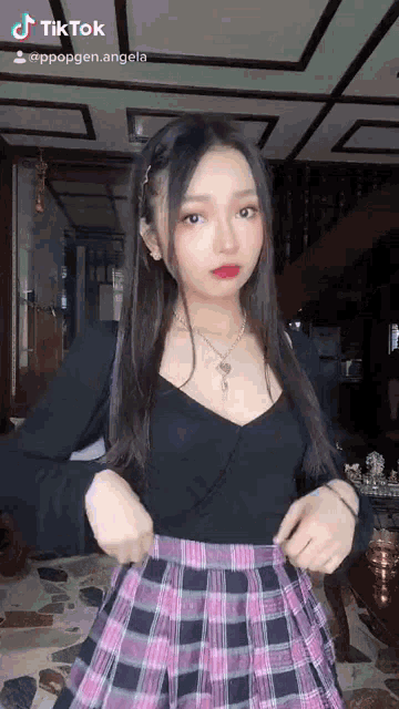 a girl in a plaid skirt and a black top is standing in a room .