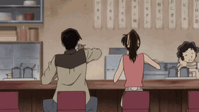 a man and a woman sit at a counter in a restaurant with chinese writing on the wall above them