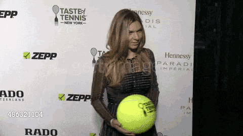 a woman holding a tennis ball in front of a wall that says taste of tennis on it