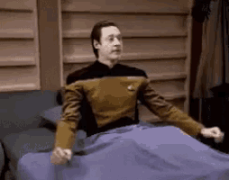a man in a star trek uniform is laying on a bed with his arms outstretched .