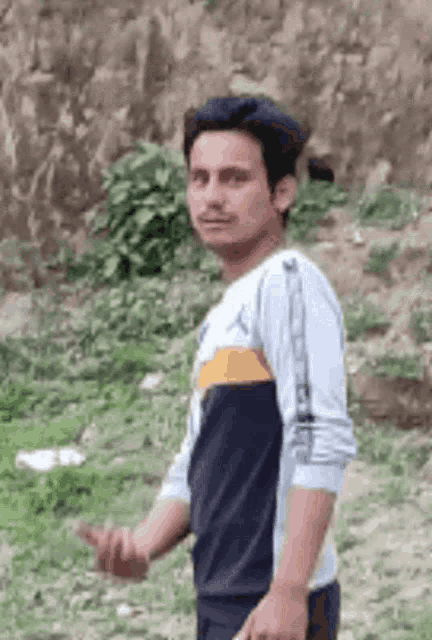 a man is standing in a field with his hands in his pockets and making a funny face .