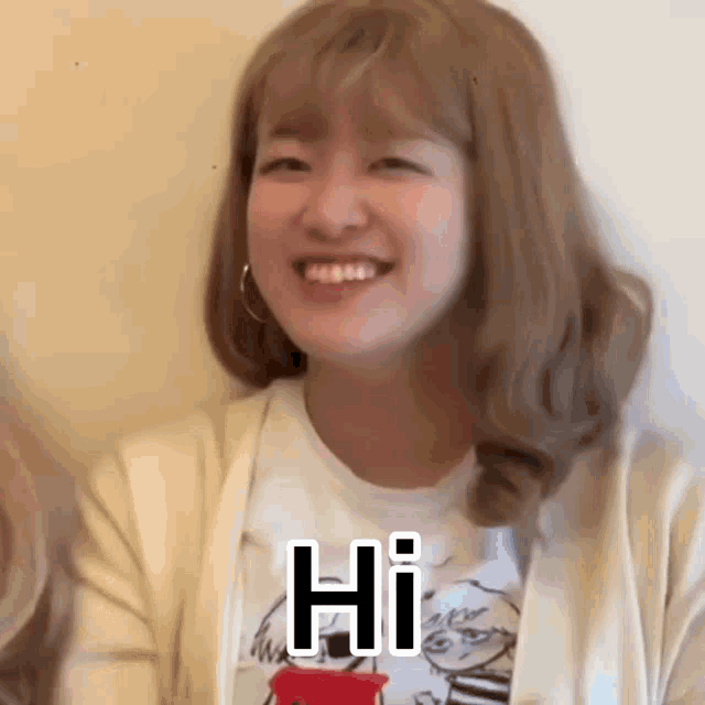 a woman is smiling and saying hi in front of a white wall .