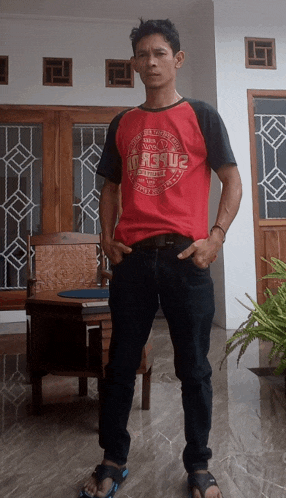 a man wearing a red shirt that says ' r3qu2 ' on it stands with his hands in his pockets