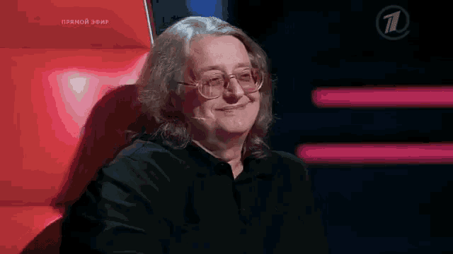 a man wearing glasses and a black shirt is sitting in a red chair and smiling .