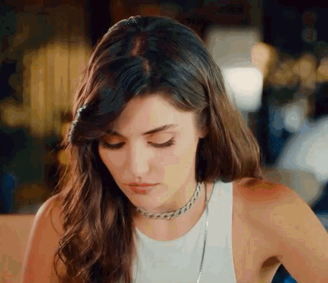 a woman wearing a white tank top and a choker looks down