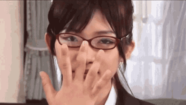 a woman wearing glasses is covering her mouth with her hand .