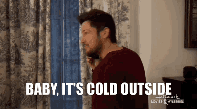 a man is standing in front of a window with the words baby it 's cold outside above him