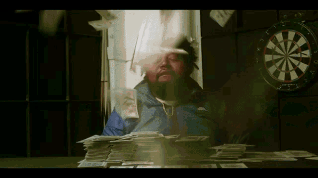 a man sitting in front of a dart board with a stack of money behind him