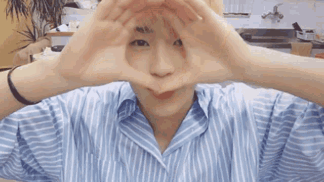 a person in a blue and white striped shirt is making a heart shape with their hands .
