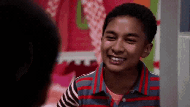 a young boy in a striped shirt is smiling while standing next to another boy in a room .