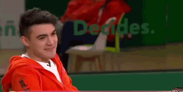a young man in a red hoodie is laughing while sitting in a yellow chair .