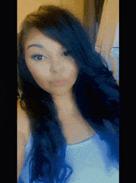 a woman with long black hair is taking a selfie in a white tank top