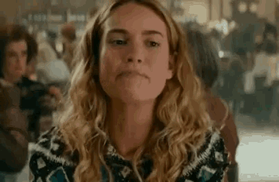 a woman with curly hair is making a funny face while sitting in a crowded room .