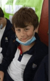 a young boy wearing a face mask is sitting in a room with other children .