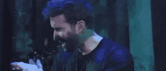 a man with a beard is standing in a dark room looking at a cell phone .