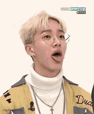 a young man with blonde hair and glasses is sticking his tongue out .