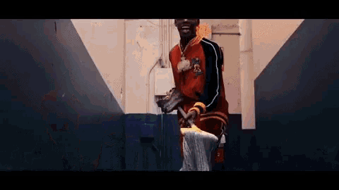 a man in a red jacket is standing in a hallway with a mop .