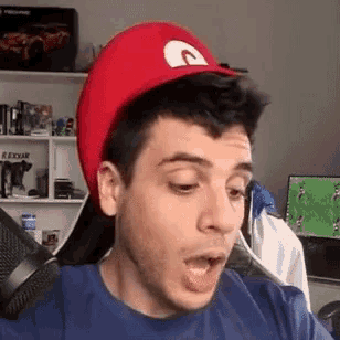 a man wearing a red hat and a blue shirt is sitting in front of a computer .