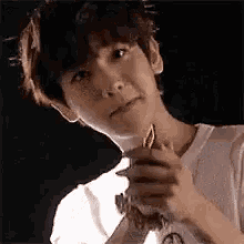 a young man in a white shirt is holding something in his hands and making a face .