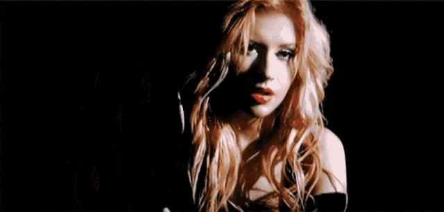 a woman with long blonde hair and red lips is standing in a dark room .