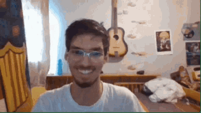 a man with glasses and a beard is smiling in front of a guitar hanging on the wall .