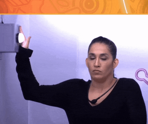 a woman in a black sweater holds her arm up in front of a wall