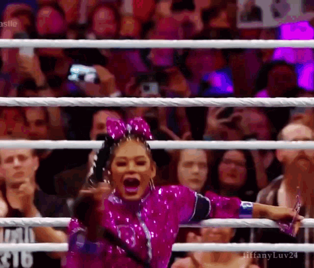 a woman in a pink suit is standing in a wrestling ring .