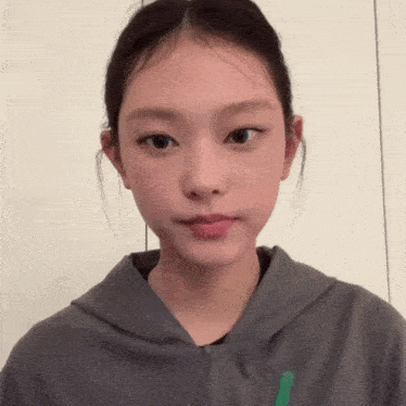 a woman wearing a grey hoodie has a green stripe on the sleeve
