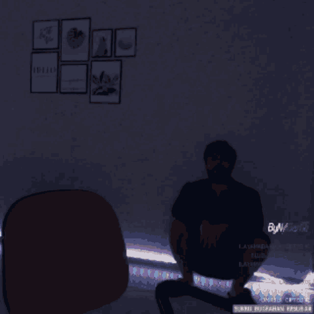 a man sits in a chair in a dark room with a few posters on the wall above him