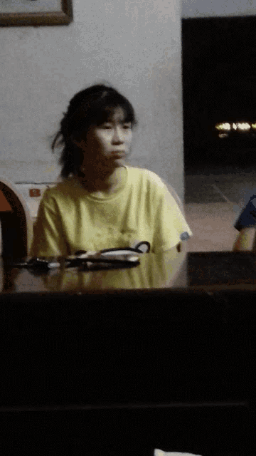 a girl in a yellow shirt sits at a table at night