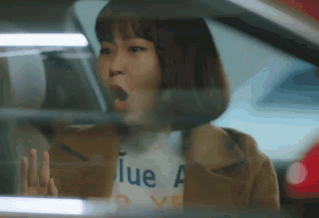 a woman in a car with her mouth open and a shirt that says blue a on it