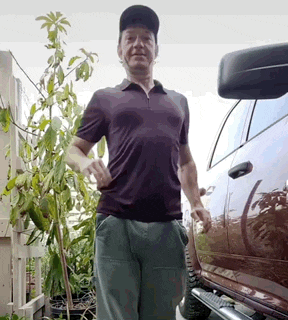 a man wearing a baseball cap is standing next to a car .